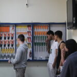 Fotografia na área interna do laboratório de Redes de Computadores. Visitantes estão de pé na frente da sala. Ao fundo, verificam-se ferramentas como chaves de fenda, alicates e outras, organizadas e dispostas em um quadro.