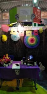 Estande decorado com fundo escuro e objetos que remete à cultura mexicana e ao Dia de los Muertos.