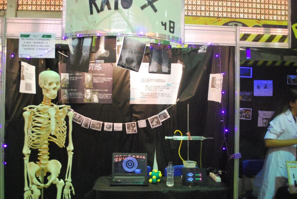 Estande decorado com imagens de raio-x. Em frente ao estande, uma réplica em tamanho real de um esqueleto humano