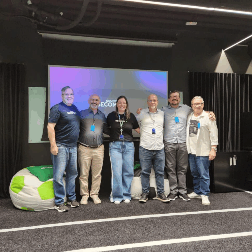 Os professores Mehram, Marco e Paulo posam para foto ao lado de três representantes da empresa Becomex, sendo dois homem e uma mulher. Eles estão de pé, lado a lado., no palco do auditório.